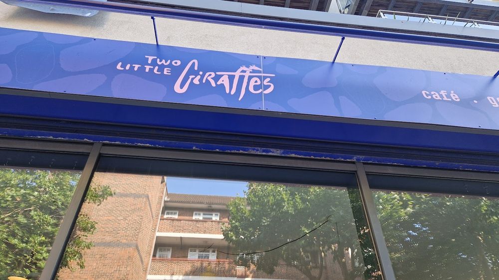 The blue shopfront of Two Little Giraffes on Thessaly Road, seen from the pavement with flats and trees behind.